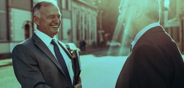 two men in suits shaking hands and smiling on the street side
