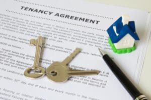 Tenancy agreement document with house keys, a miniature house, and a pen on top, representing a rental or lease agreement.