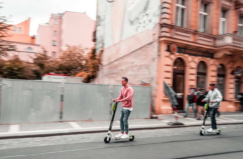 An image of two men riding scooters down a street.