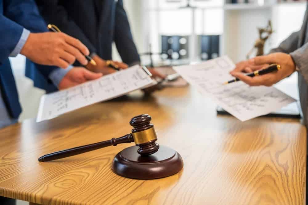 A group of business professionals and a lawyer in formal attire are seated around a desk, engaged in a meeting. They are discussing a contract, focusing on legal aspects and litigation matters.
