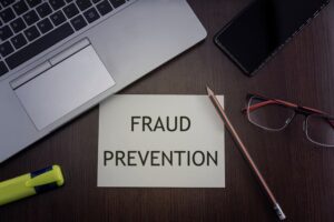Top view of office table desktop background with laptop, phone, glasses and pencil with card with inscription fraud prevention.