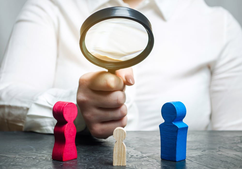 Person holding magnifying glass between mother, father, and child figures, symbolizing paternity determination in Florida