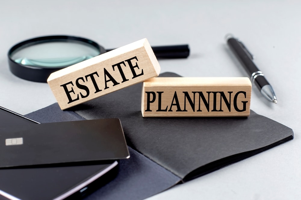 Wooden blocks reading “Estate Planning” on a desk with documents and pen