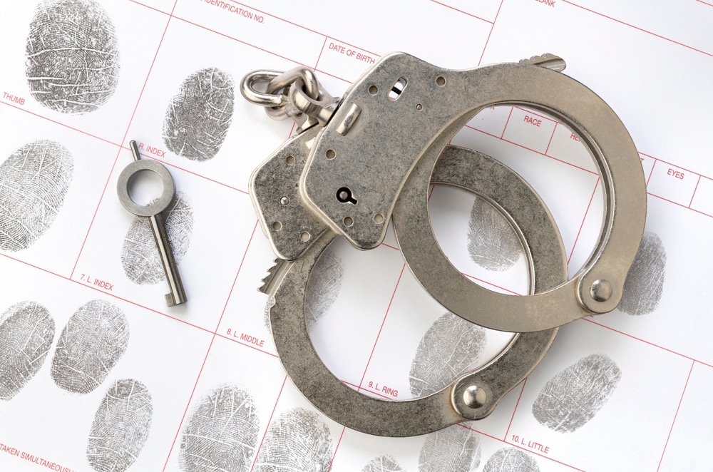 Metal handcuffs placed on fingerprint form, symbolizing a criminal record.