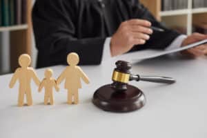 Wooden figures of parents and child with a judge and gavel in the background, symbolizing custody and relocation decisions.