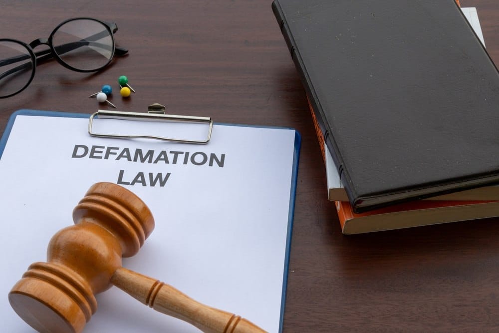 Clipboard labeled "Defamation Law" with a gavel, glasses, and law books on a desk