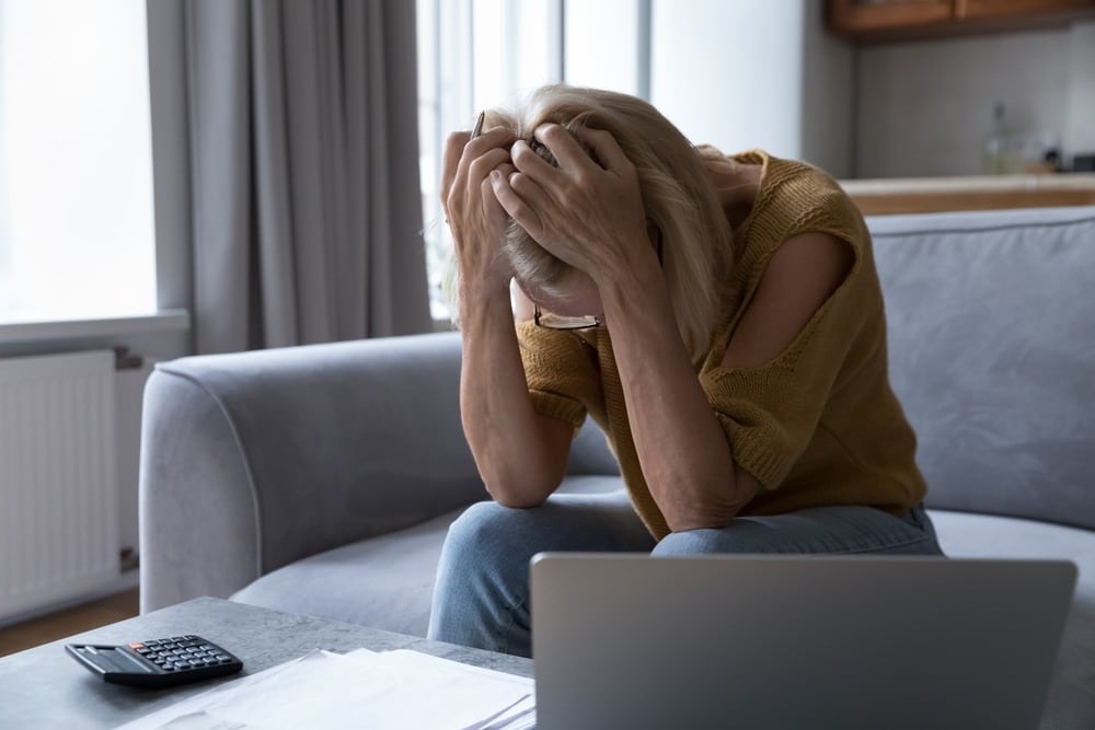Woman sitting on a couch with her head in her hands next to a calculator and laptop